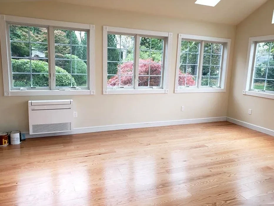 Bright sunroom with refinished wide-plank hardwood floors and large windows